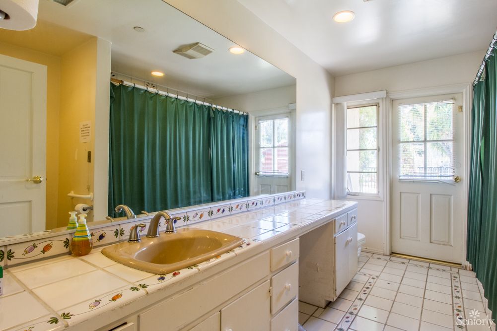A spacious bathroom with a long countertop, large mirror, and green shower curtain.