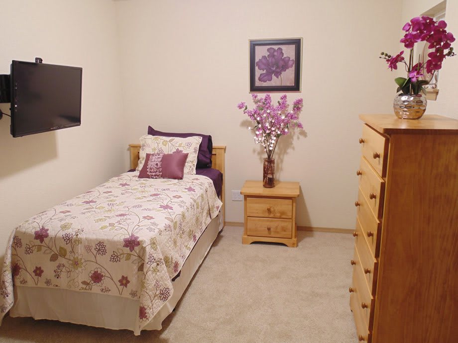 A cozy bedroom with a single bed adorned with floral bedding, matching wall art, and wooden furniture.