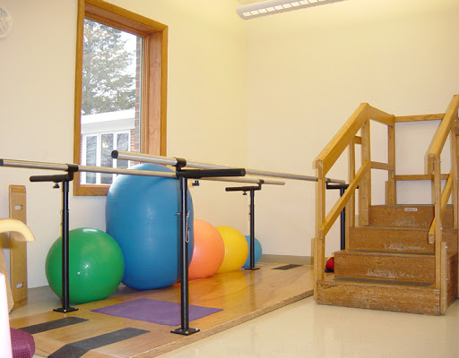 A well-equipped therapy room featuring balance bars, a staircase, and colorful exercise balls.