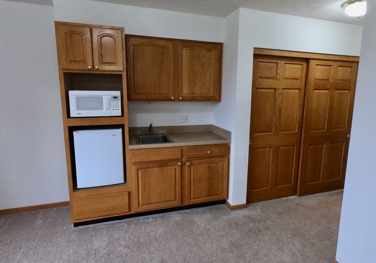 Compact kitchenette setup with wooden cabinets, a microwave, mini fridge, and a sink.