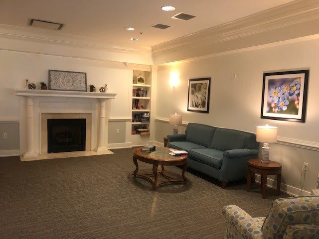 A cozy living room with a couch, coffee table, and fireplace, adorned with artwork and a bookshelf.