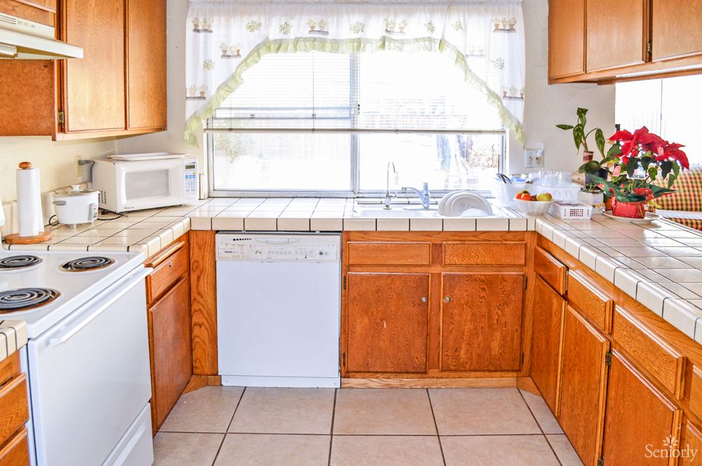 A bright kitchen with wooden cabinets, a dishwasher, and a large window.
