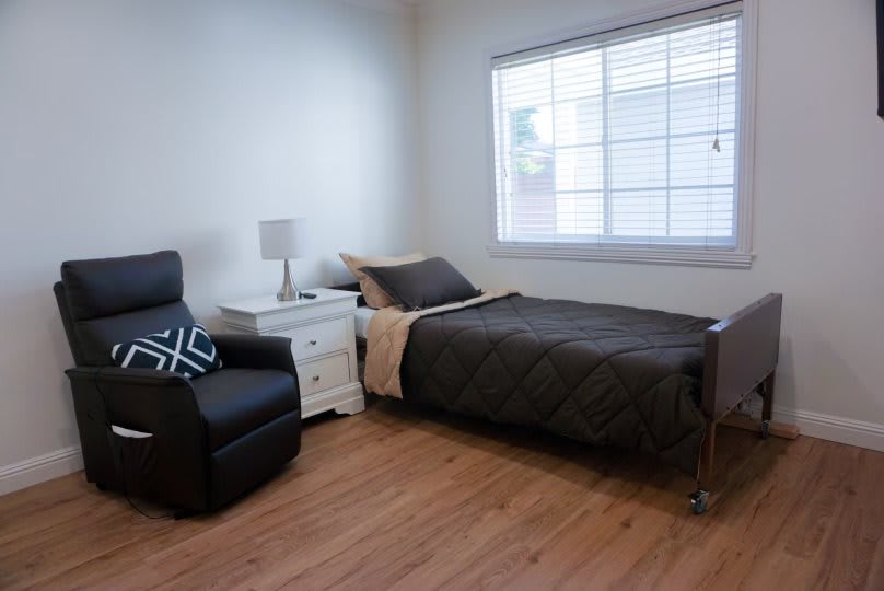 A minimalist bedroom with a single bed, armchair, and nightstand.