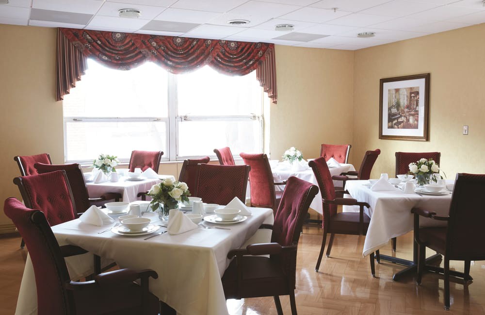 An elegantly set dining area with neatly arranged tables and chairs, featuring white tablecloths and floral centerpieces.