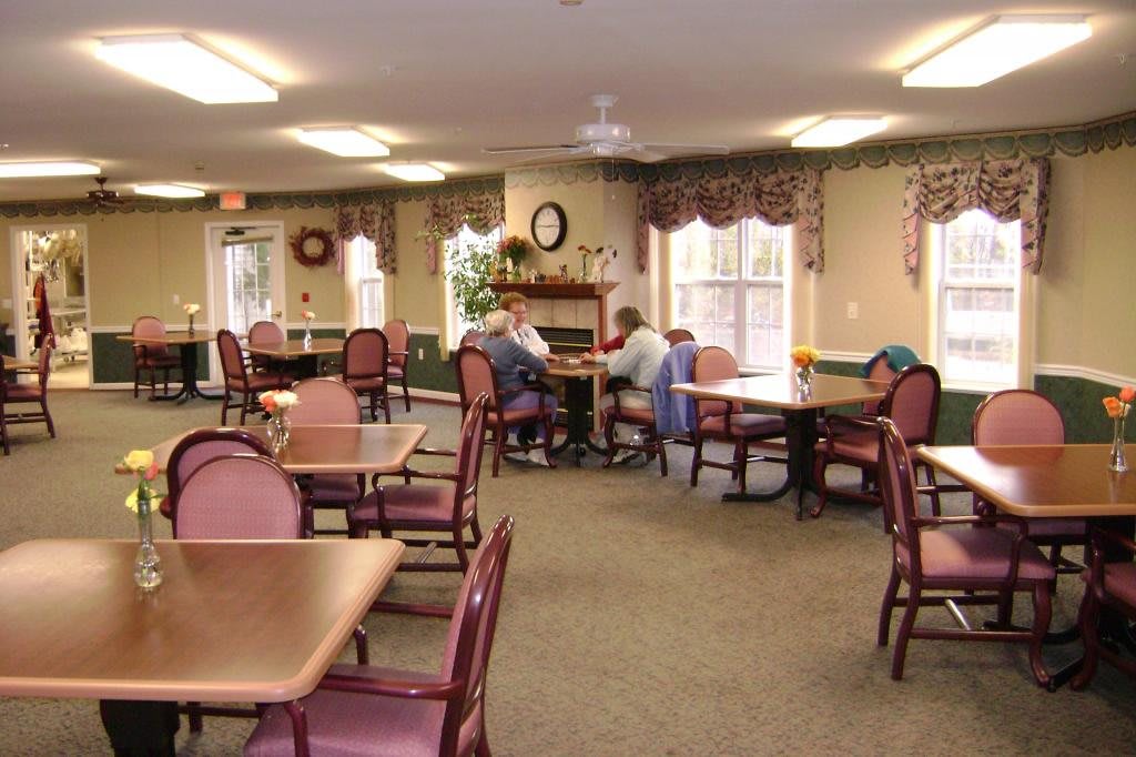 A communal dining area with tables and chairs where people are gathered for a meeting.