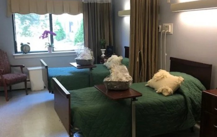 A hospital room with two beds, green covers, and a view of the window with light filtering in.