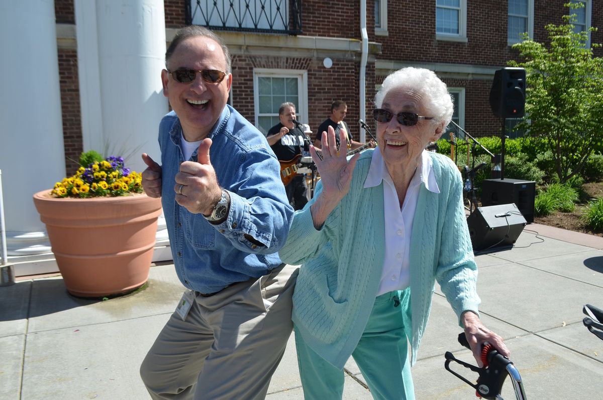 An elderly woman and a man are smiling and waving while enjoying the outdoors.