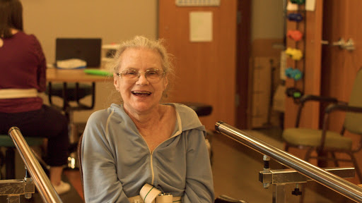 An elderly woman smiles joyfully while seated in a care facility.