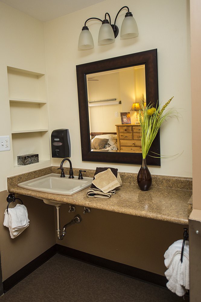 A bathroom counter with a sink, mirror, and decorative vase with flowers.