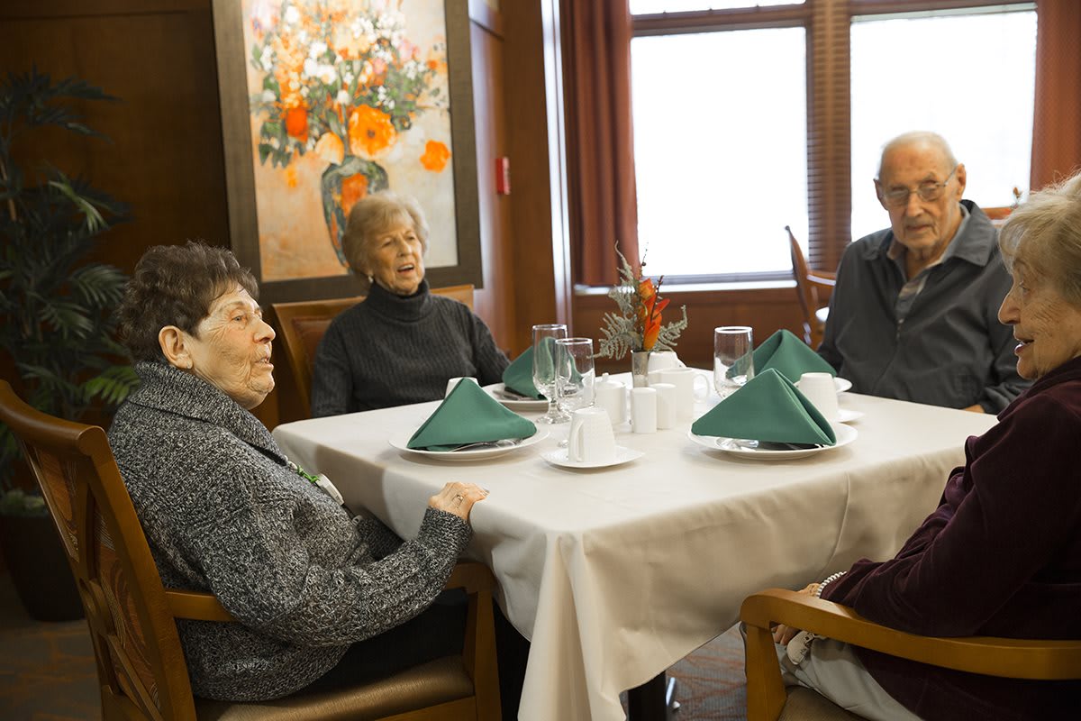 A group of seniors sitting around a dining table with formal place settings.