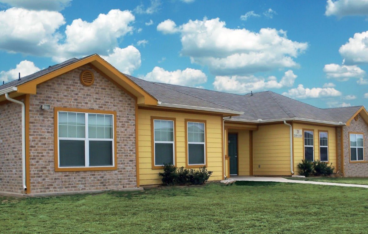 A suburban house with brick and yellow siding under a cloudy sky.