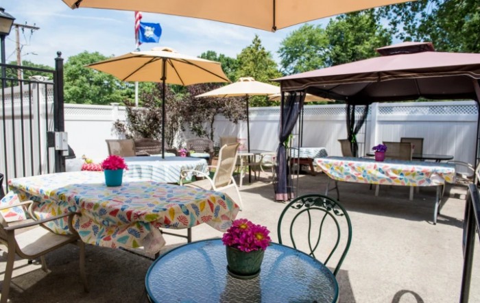 A cozy outdoor patio area featuring tables with umbrellas, colorful flowers, and a gazebo.