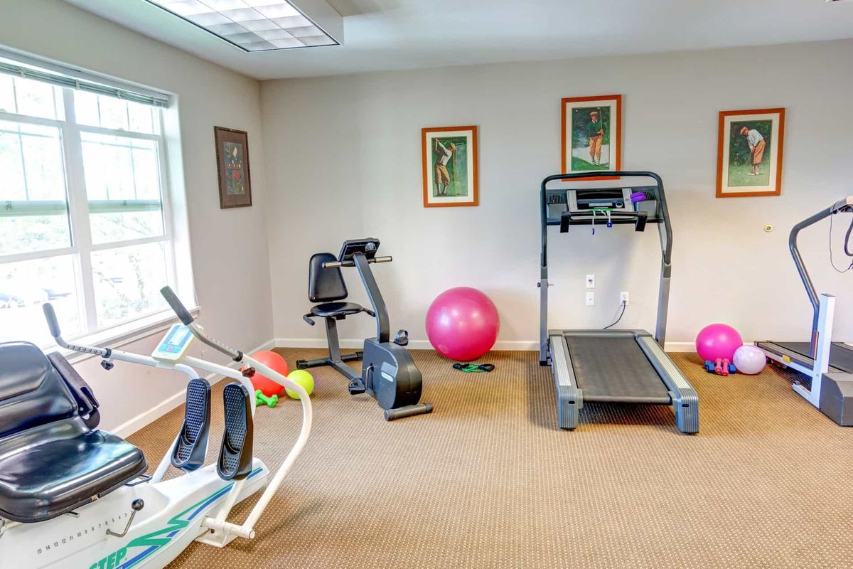 A compact home gym with various exercise equipment including a treadmill, stationary bike, elliptical machine, and an exercise ball.