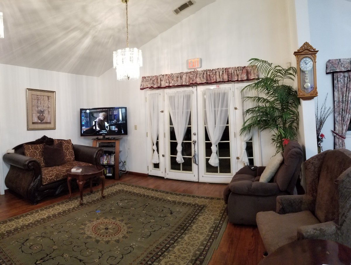 A cozy living room featuring a television, sofas, curtains, and a chandelier.