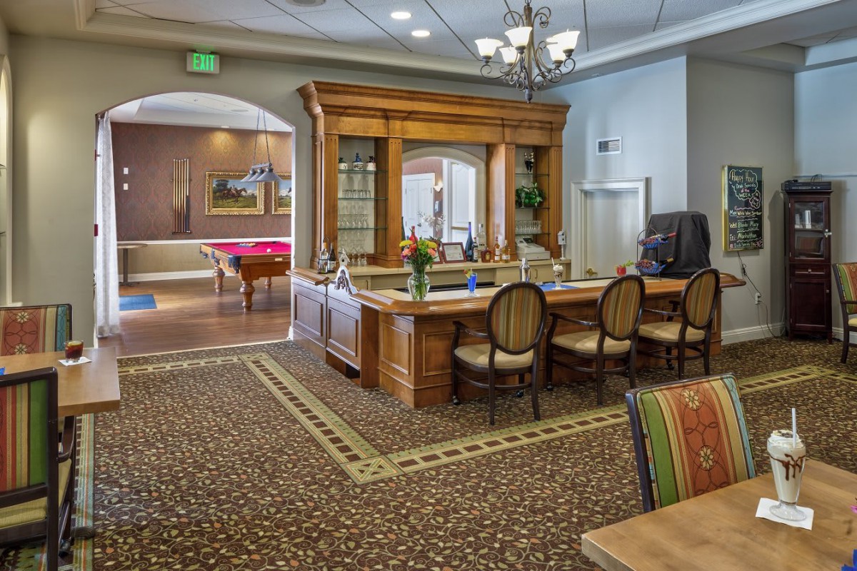 A cozy interior featuring a wooden bar with seating, a billiard table, and elegant lighting.