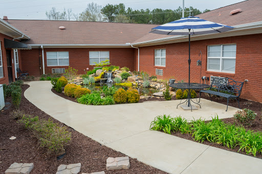 A beautifully landscaped outdoor area featuring a winding pathway, vibrant flowers, and a shaded seating area with an umbrella.