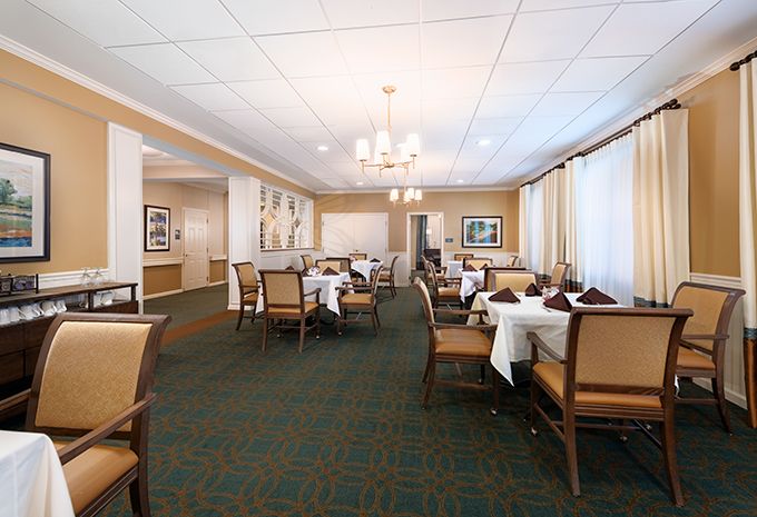 A spacious dining room with neatly arranged tables and chairs, featuring large windows and elegant chandeliers.