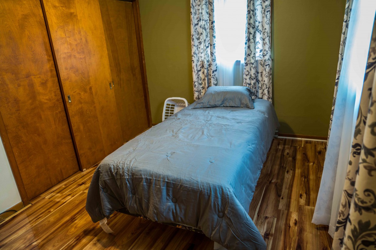 A cozy bedroom with a single bed, wooden floor, and patterned curtains.