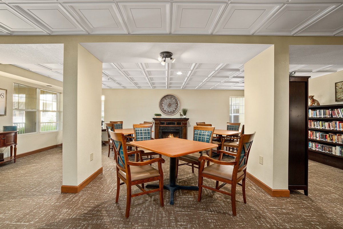 A cozy dining area with wooden tables and chairs, featuring a carpeted floor and ceiling light fixtures.