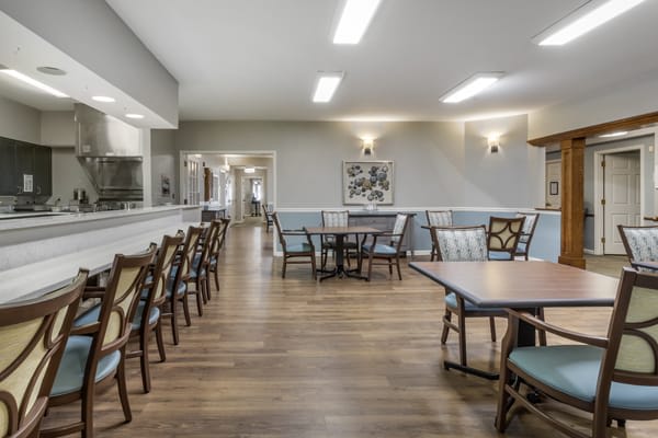 A well-lit dining area with wooden floors, containing several tables and chairs.