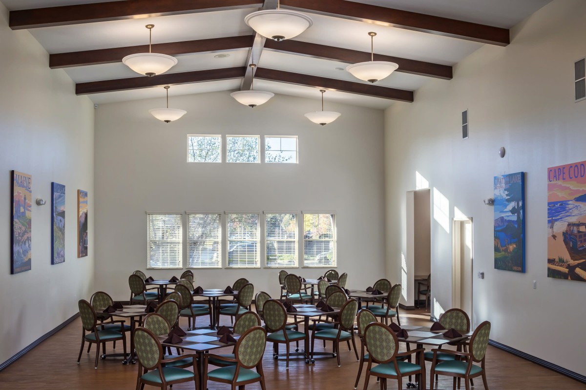 A bright dining area with multiple tables and chairs arranged neatly under ceiling lights.