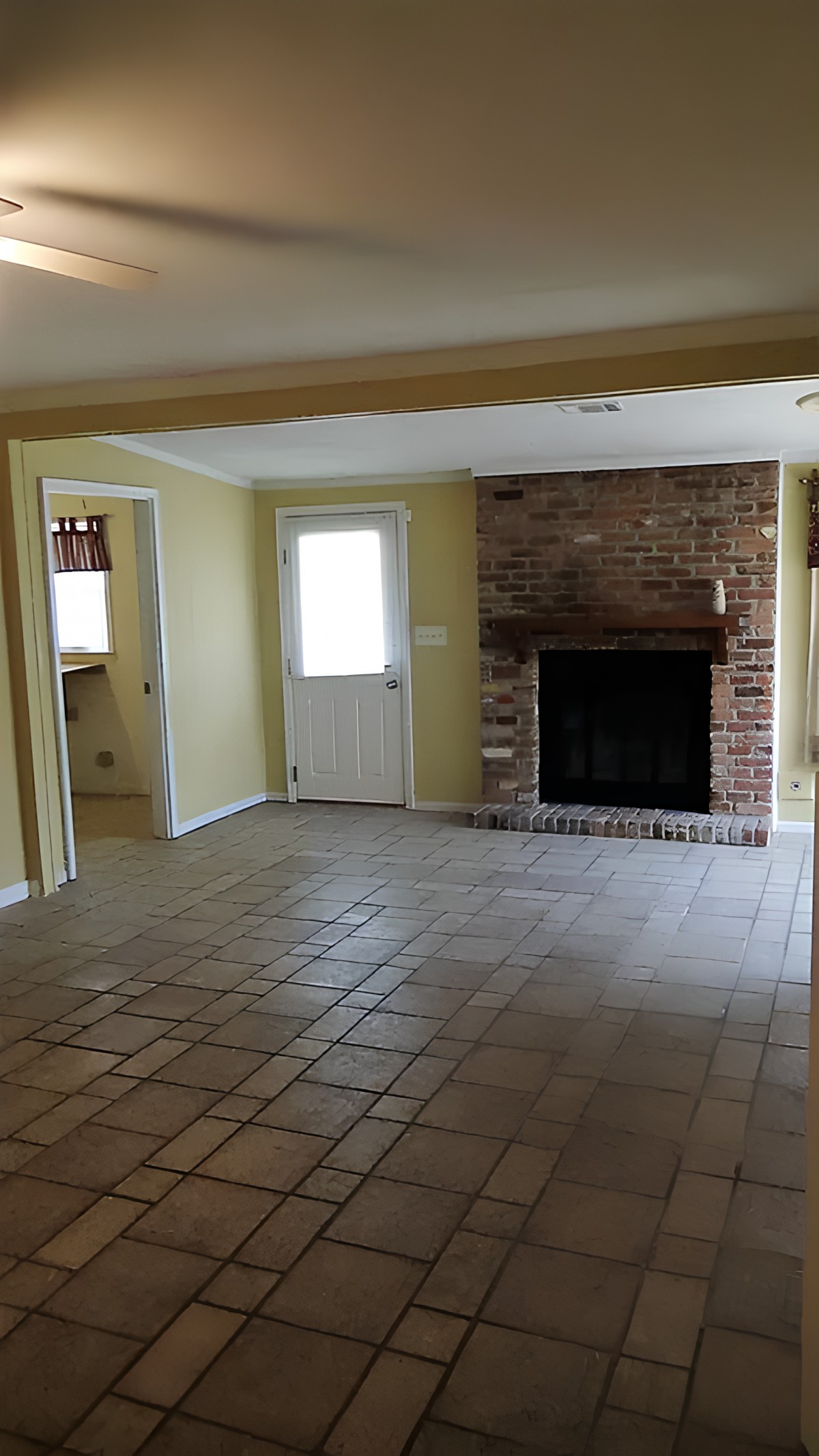 An empty living room with a brick fireplace and tiled floor.