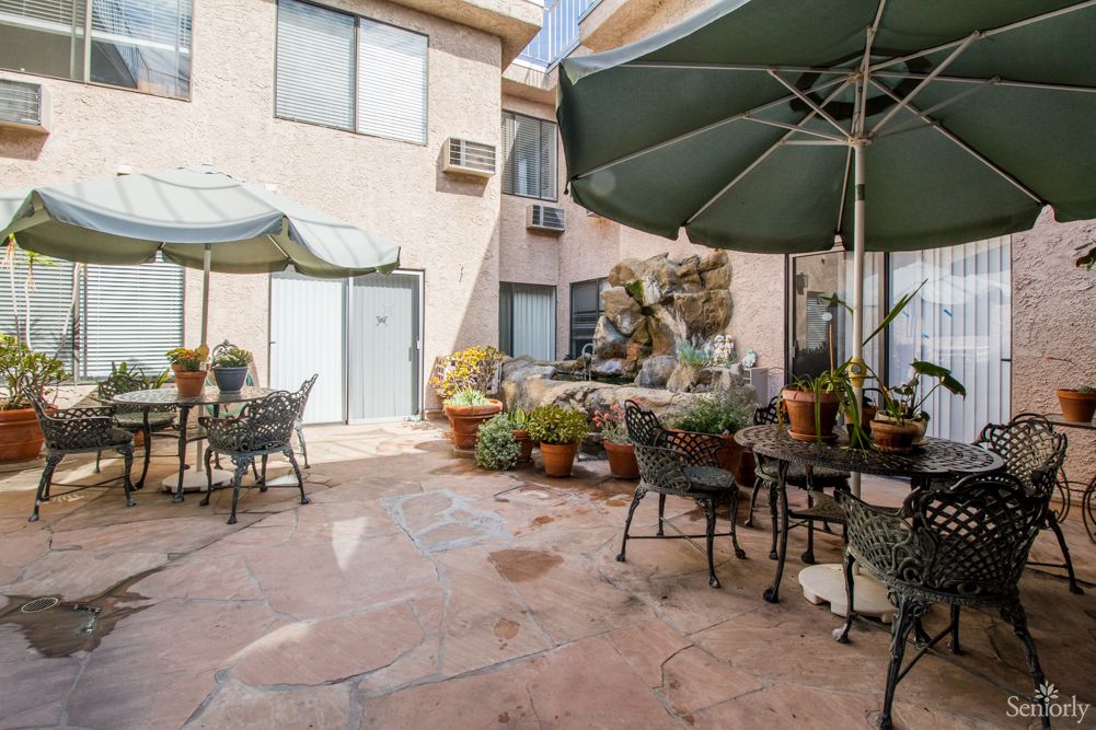 A charming courtyard patio with tables, chairs, umbrellas, and an abundance of potted plants.