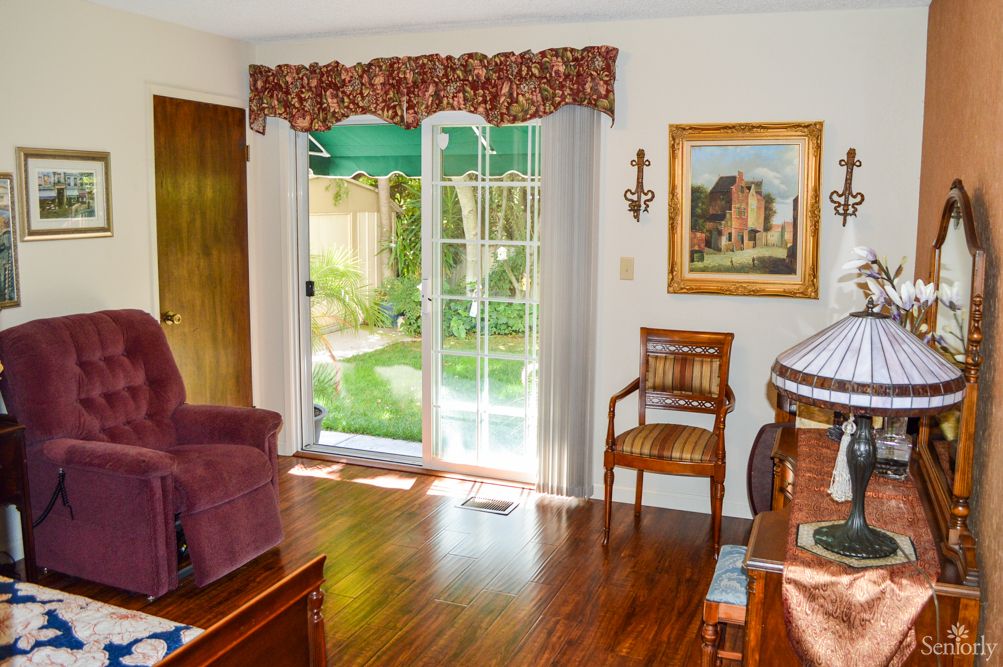 A cozy living room with a plush armchair, wooden floors, and natural light streaming through a sliding glass door.