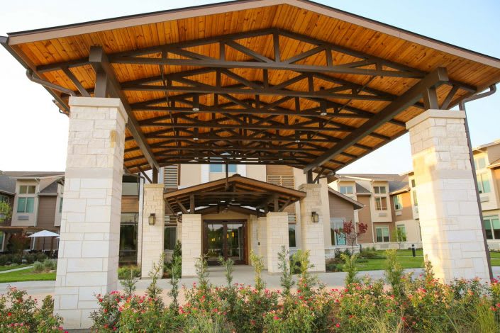 A modern building entrance with a wooden roof structure and landscaped surroundings.
