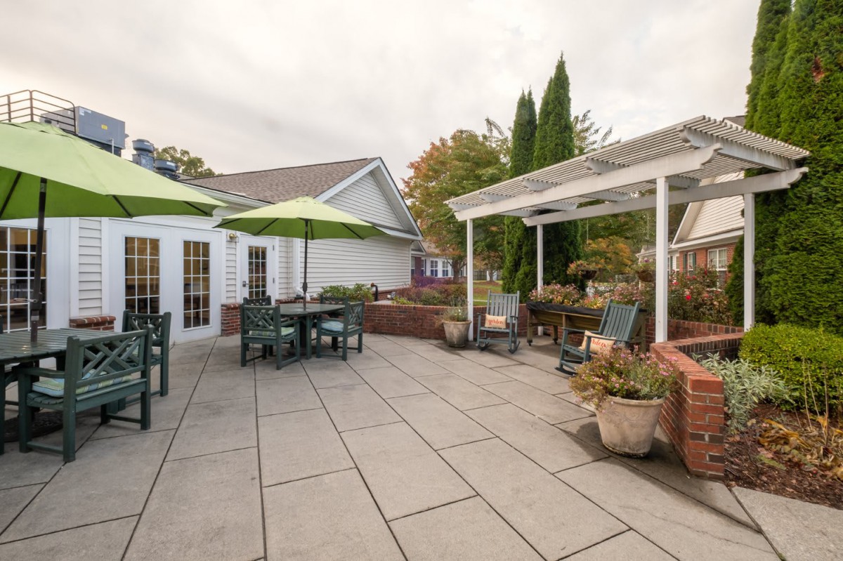 A spacious outdoor patio with furniture, green umbrellas, and a pergola adorned with plants.