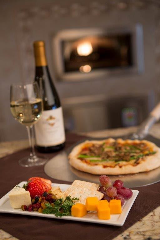 A gourmet meal featuring a freshly baked pizza, a cheese platter with fruits, and a bottle of white wine.