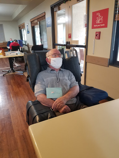 A senior person sitting comfortably in a chair, wearing a mask in an indoor setting.