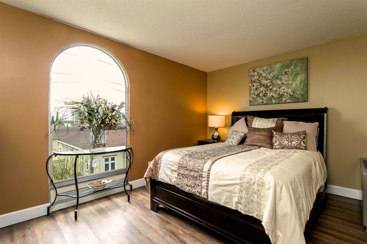 A well-decorated bedroom featuring a comfortable bed, soft lighting from a bedside lamp, and a large window with an arched frame.