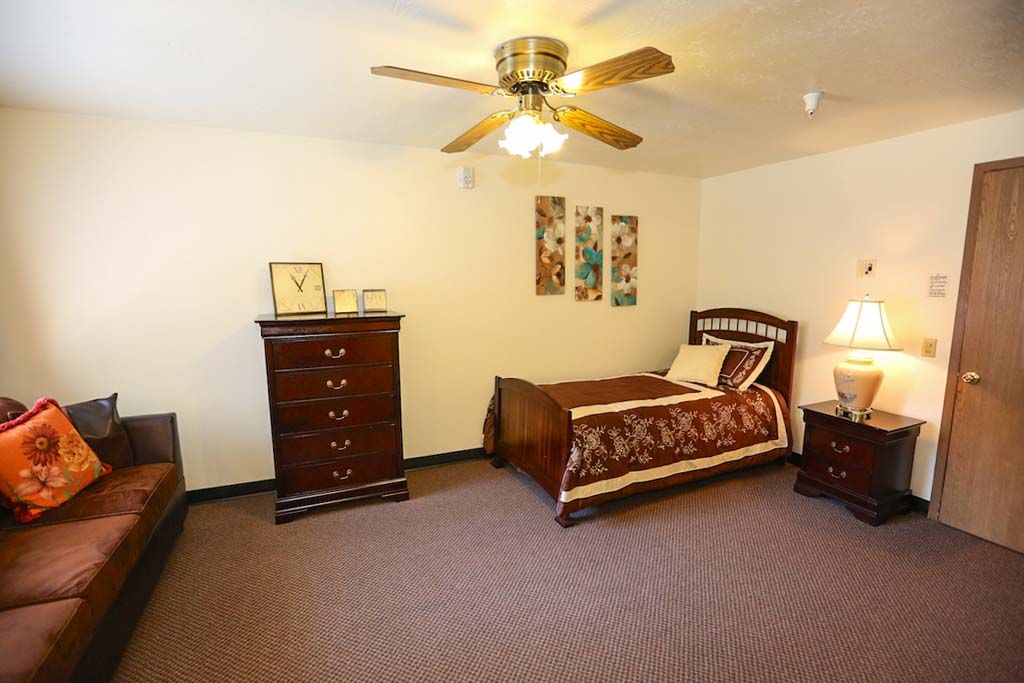 A cozy bedroom featuring a single bed, dresser, and ceiling fan.