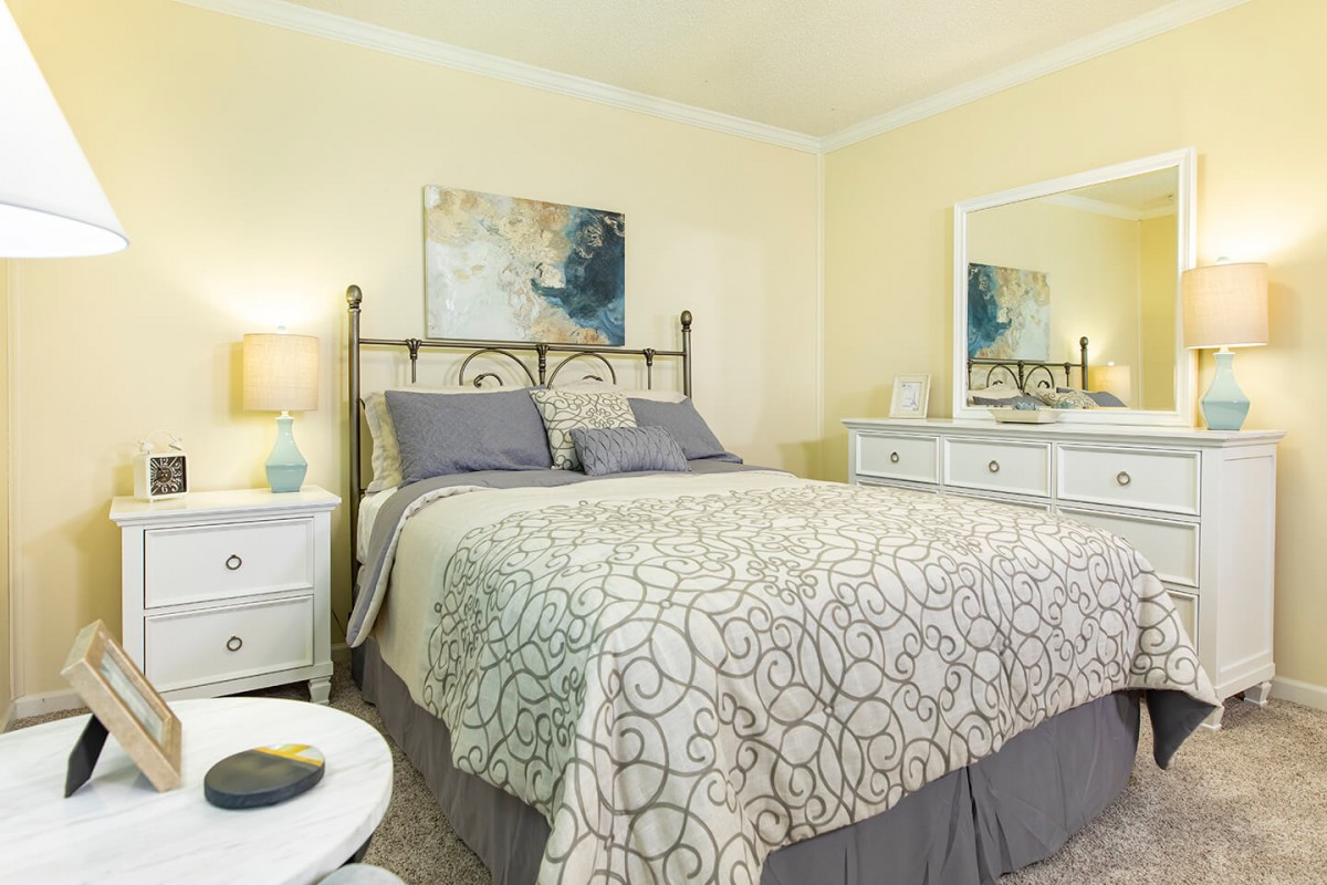 A cozy and well-decorated bedroom with a bed, nightstand, and dresser, featuring soft lighting and artwork on the walls.