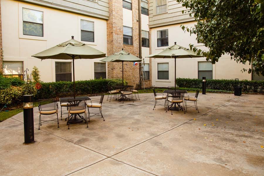 An outdoor patio area with tables, chairs, and umbrellas in an apartment complex.