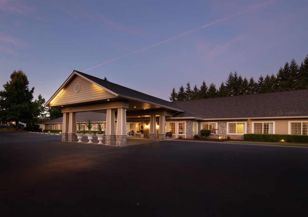 An illuminated building exterior during the evening, surrounded by forested landscape.