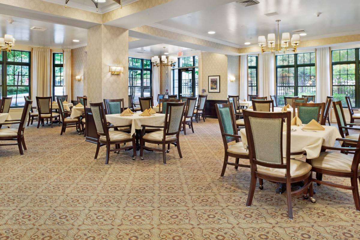An elegant dining area with neatly arranged tables and chairs, featuring a carpeted floor and chandeliers overhead.