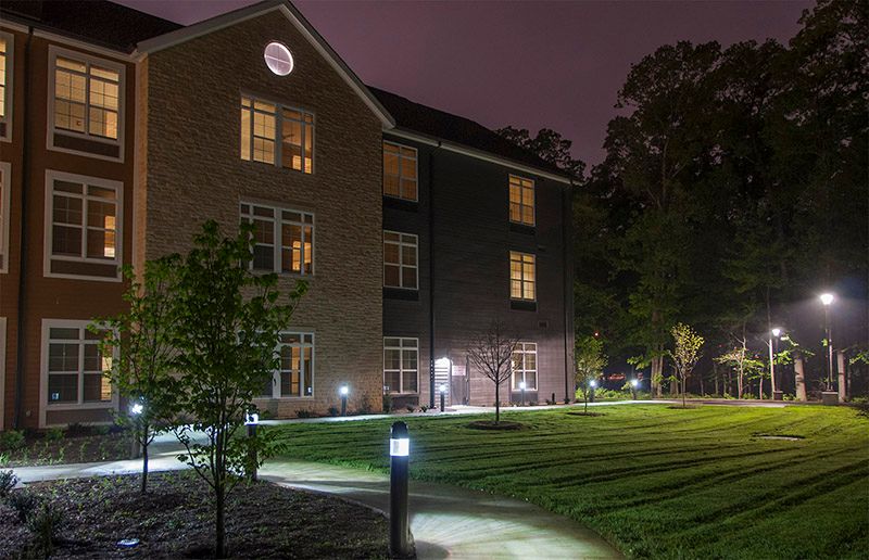 A well-lit building at night with a grassy area and pathway.
