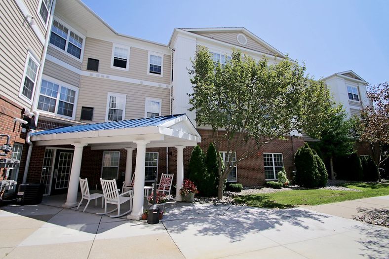 A sunny day view of a residential apartment building with a patio area and surrounding trees.