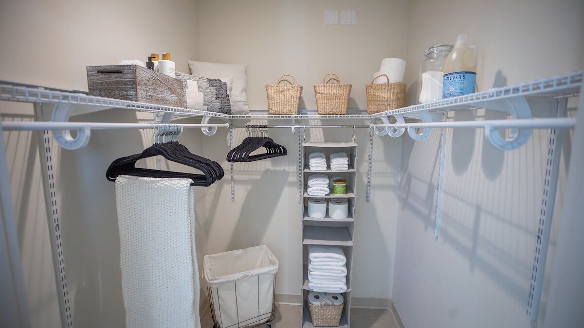 A well-organized closet with shelves holding towels and baskets, alongside hangers and a laundry basket.