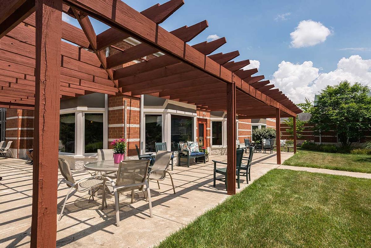 A backyard patio featuring a wooden pergola over outdoor seating and a table, adjacent to a brick house.