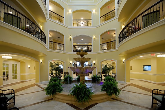 A spacious indoor atrium with balconies, featuring a central fountain surrounded by greenery.