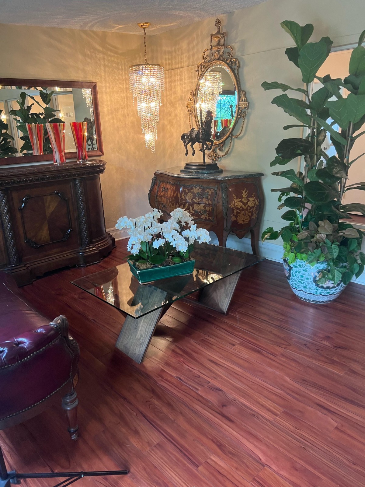A cozy living room with elegant furniture and decor, featuring a glass coffee table, plants, and warm lighting.