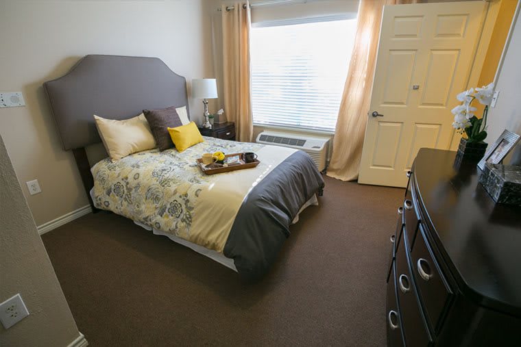 A cozy and well-decorated bedroom with a neatly made bed, pillows, and a tray, complemented by natural light streaming through the window.