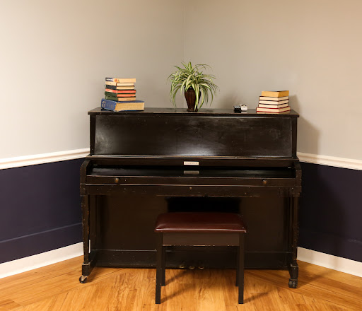 A classic black piano with a cozy setup, adorned with books and a small plant.