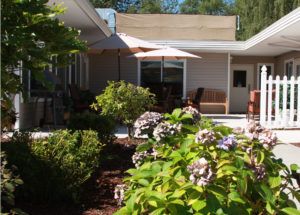 A well-maintained garden with blooming flowers next to a patio area in front of a house.
