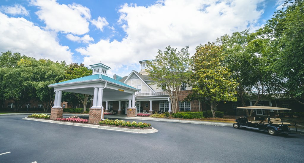 A well-maintained building entrance surrounded by trees under a partly cloudy sky.