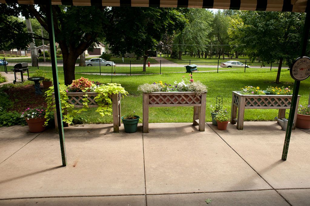 A patio with planters overlooking a green lawn and trees.