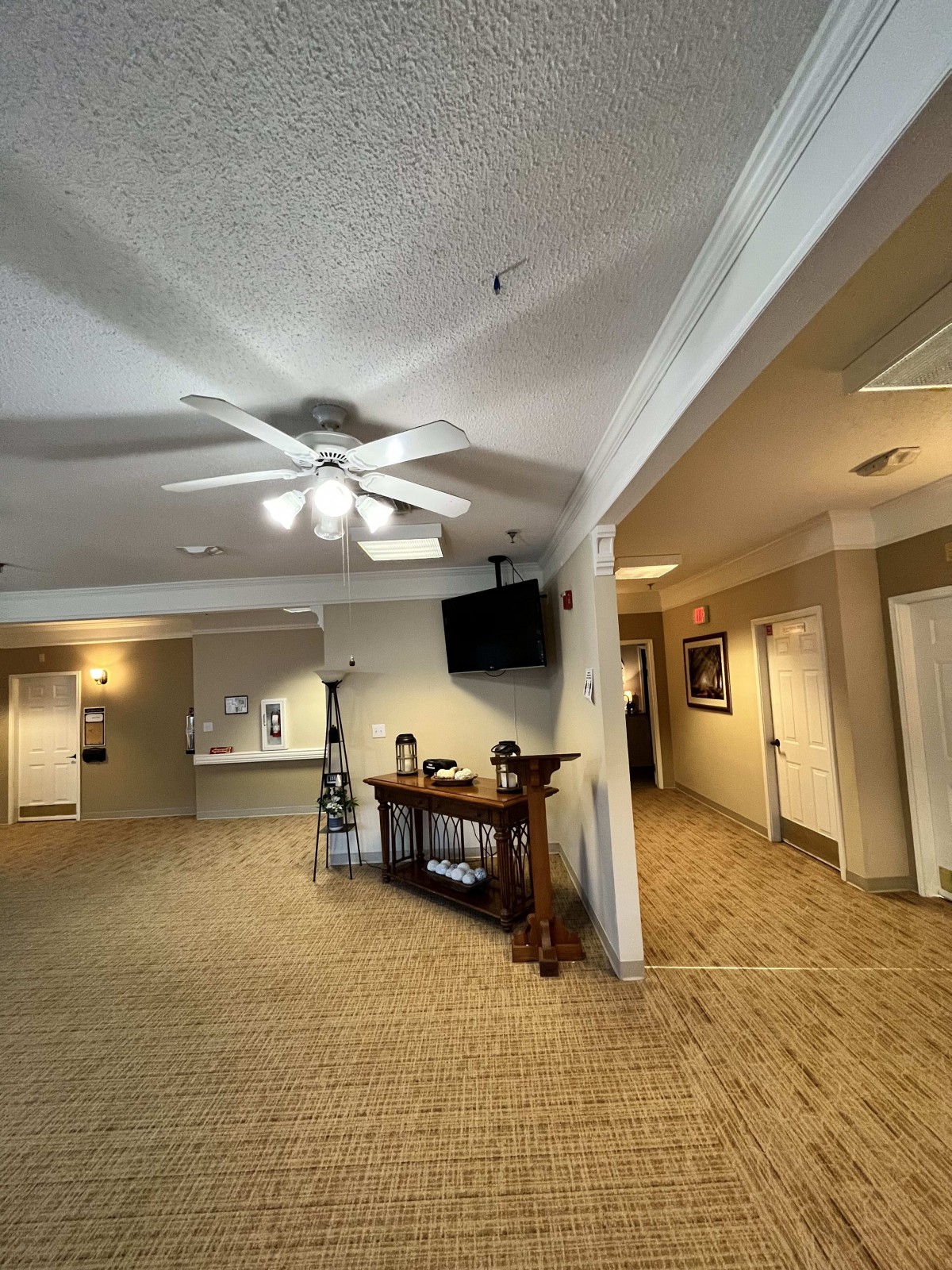 A spacious lobby area with a reception desk, hallway, ceiling fan, and television.
